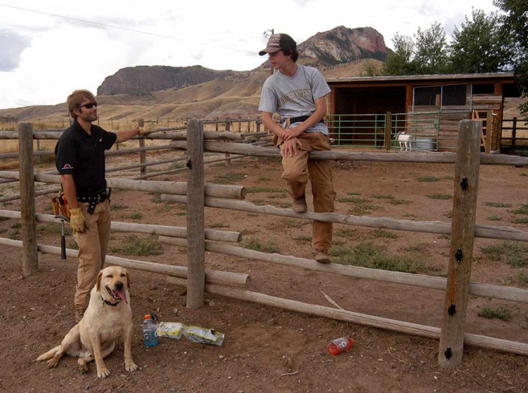P.J. Schneider, left, and dog dexter take a break while installing an electric fence last month with Russ Talmo. Defenders of wildilfe helped Schneider with cost-sharing and tehnical expertise on the project at a ranch southwest of Cody, Wyo. where chickens and goats could attract grizzly bears.