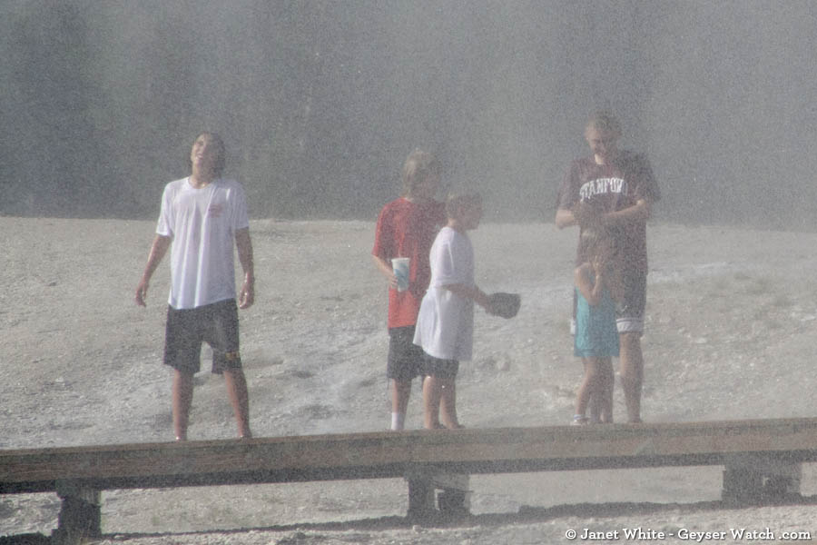 A family stands in the spray from Beehive Geyser in Yellowstone Park. (Janet White/Geyser Watch - click to enlarge)