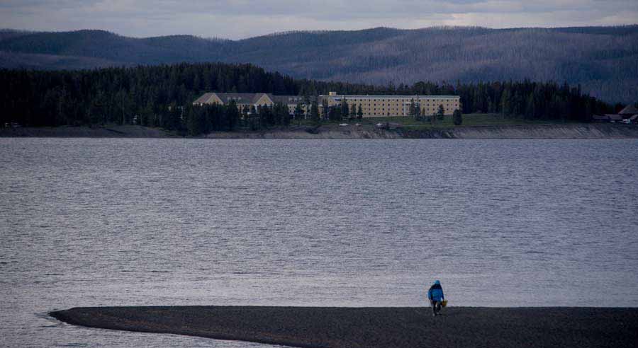 A beachcomber walks along the shore of Yellowstone Lake in view of Lake Hotel as the evening light fades in Yellowstone National Park. (Ruffin Prevost/Yellowstone Gate)