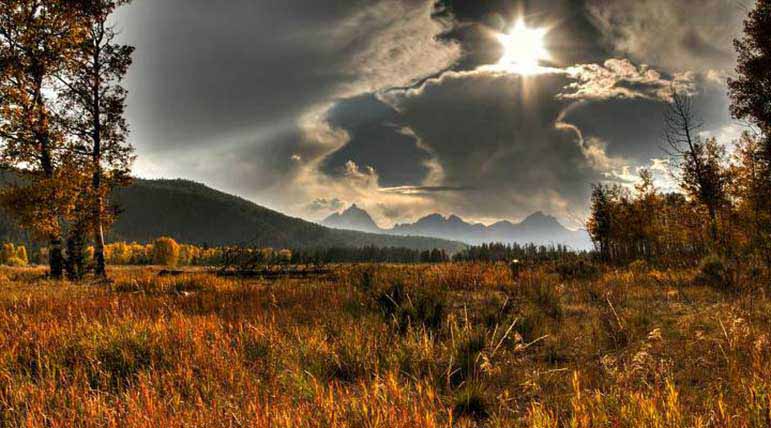 The Tetons rise in the distance over a scenic valley.