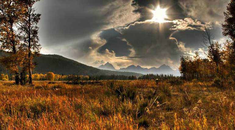 The Tetons rise in the distance over a scenic valley.