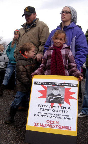 Jordan Howard, 7, holds a protest sign in front of her mother, Rachel Howard, of Cody, Wyo. They were among approximately 75 protestors who gathered at the East Gate to Yellowstone National Park on Sunday to demand a solution to the federal government shutdown that has closed national parks nationwide.