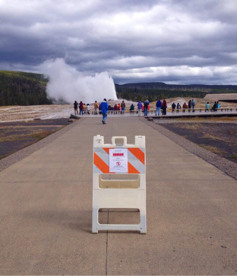 About two dozen visitors to Yellowstone National Park watch Old Faithful Geyser erupt Tuesday afternoon despite a sign advising that the attraction is closed in the wake of a federal goverment shutdown. No visitors were allowed into national parks Tuesday, while those already inside park boundaries will be asked to leave. 