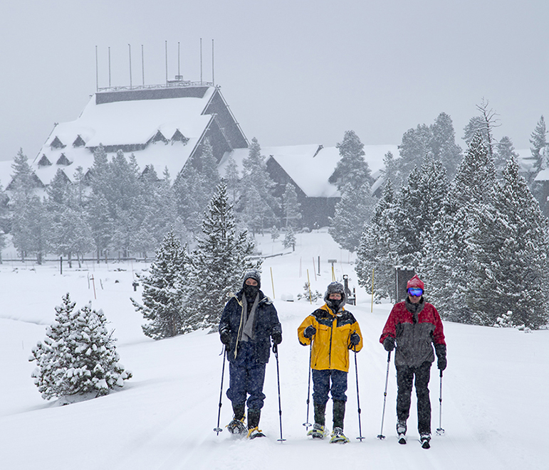 Old Faithful Inn is visible in the background as winter travelers in Yellowstone National Park head out for a trip to Black Sand Pool.