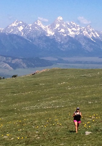 The Tetons loom in the background as hiker Cara Rank walks through a grassy meadow on Sheep Mountain in Jackson Hole.