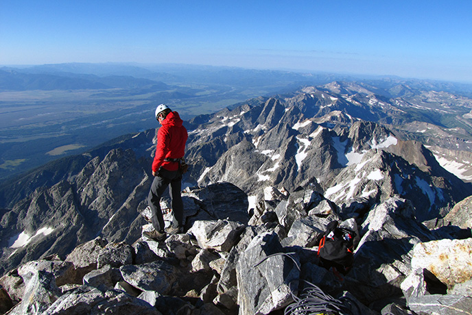 A climber on the summit of the Grand Teton in Grand Teton National Park surveys the Jackson Hole valley below.